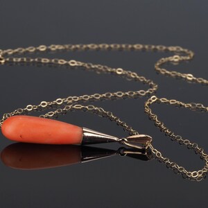 Pu&ograve; includere: Una collana a catena dorata con un ciondolo liscio e allungato a forma di goccia in corallo arancione. Il pezzo di corallo &egrave; sormontato da una montatura in metallo dorato lucido che si collega alla sottile catena a maglie dorate.