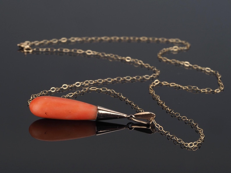 Pu&ograve; includere: Una collana a catena dorata con un ciondolo liscio e allungato a forma di goccia in corallo arancione. Il pezzo di corallo &egrave; sormontato da una montatura in metallo dorato lucido che si collega alla sottile catena a maglie dorate.