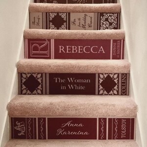 May include: A staircase with beige carpeted treads and risers decorated with book spine decals. The decals feature titles including Far from the Madding Crowd, Rebecca, The Woman in White, and Anna Karenina in maroon and white.