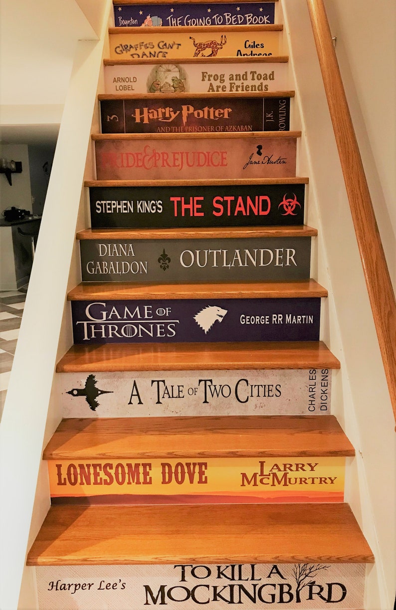 May include: A staircase with risers decorated to resemble book spines, featuring titles such as The Going to Bed Book, Harry Potter, Pride and Prejudice, The Stand, Outlander, Game of Thrones, A Tale of Two Cities, Lonesome Dove, and To Kill a Mockingbird.