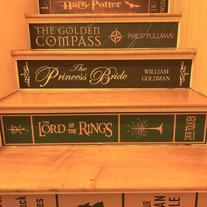 May include: A wooden staircase with risers decorated to resemble book spines. Titles include Harry Potter and the Sorcerer's Stone, The Golden Compass, The Princess Bride, The Lord of the Rings, and The Adventures of Sherlock Holmes.