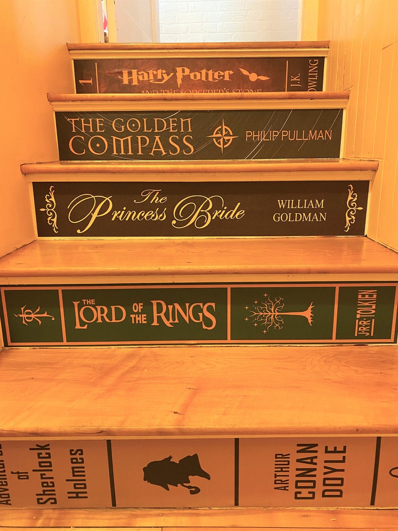 May include: A wooden staircase with risers decorated to resemble book spines. Titles include Harry Potter and the Sorcerer's Stone, The Golden Compass, The Princess Bride, The Lord of the Rings, and The Adventures of Sherlock Holmes.