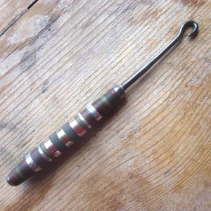 Peut inclure: Un crochet en métal avec une poignée rayée brune et argentée. Le crochet est utilisé pour tirer des objets à travers de petites ouvertures.
