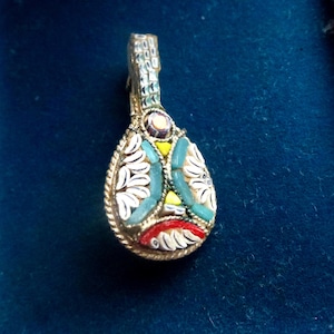 May include: A small, ornate pendant shaped like a mandolin. It has a mosaic design with turquoise, white, yellow, and red elements, set in a gold-toned metal frame. The top has a detailed, textured design.