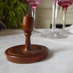 May include: A wooden goblet stand with a round base and a tall, pointed top. The stand is made of dark brown wood and has a smooth finish.