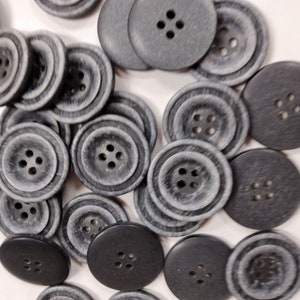 May include: A collection of gray and black buttons with four holes each. The buttons are made of a textured material and have a slightly worn look.
