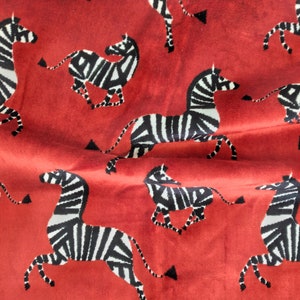 May include: Red fabric with a repeating pattern of black and white zebras. The zebras are facing different directions and are in various positions.