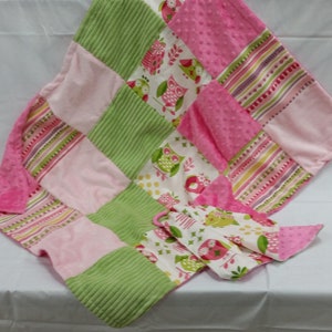 May include: A patchwork baby blanket with pink, green, and patterned squares. The blanket has a soft texture, an owl print, and striped details. A matching burp cloth is also included.