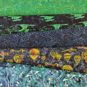 May include: Five different fabric swatches with various patterns. The top swatch is green with a white swirl pattern. The second swatch is black with a white swirl pattern and green airplanes. The third swatch is blue with a white swirl pattern. The fourth swatch is black with a white swirl pattern and colorful hot air balloons. The bottom swatch is green with a white swirl pattern and blue kites.