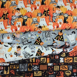 May include: Fabric with a Halloween theme featuring orange pumpkins and various cat characters dressed in costumes. The cats are depicted as skeletons, ghosts, and witches. The fabric also includes bats and stars.