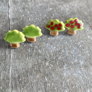 Peut inclure: Trois décorations d'arbre en céramique. Deux sont vertes avec des troncs bruns et les deux autres sont vertes avec des troncs bruns et des points rouges.