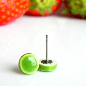 Peut inclure: Une paire de boucles d'oreilles clous en céramique verte avec des tiges argentées. Les boucles d'oreilles sont rondes et ont une finition brillante.