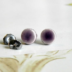 Può includere: Un paio di orecchini a perno d'argento con cime rotonde in ceramica viola e bianca.