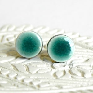 Op de afbeelding: Een paar tealblauwe keramische oorbel studs. De oorbellen zijn rond en hebben een witte rand.
