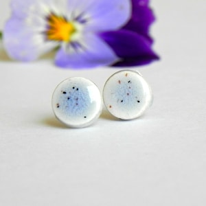 Puede incluir: Un par de pendientes de botón de cerámica blanca con motas azules y marrones.