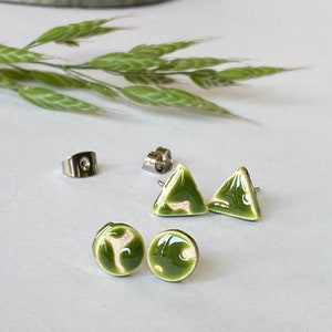 Pode incluir: Uma coleção de brincos de cerâmica em várias formas. Os brincos incluem dois pares de brincos de botão redondos e dois pares de brincos triangulares. Os brincos são esmaltados em verde brilhante com detalhes brancos. As costas dos brincos também são visíveis.