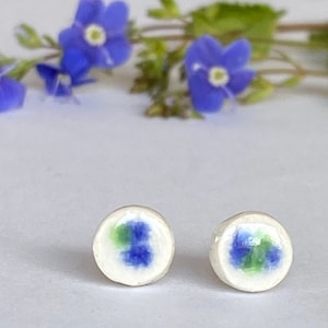 May include: A pair of white ceramic stud earrings with blue and green floral designs.