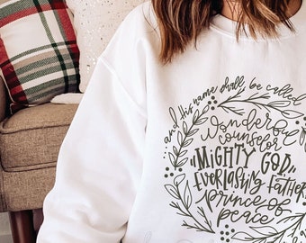 May include: White sweatshirt with a black hand-lettered design that reads "And his name shall be called Wonderful Counselor, Mighty God, Everlasting Father, Prince of Peace" with the scripture reference "Isaiah 9:6".