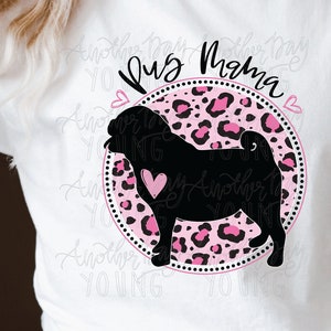 Può includere: Una maglietta bianca con un design a silhouette di carlino rosa e nero. Il design include il testo "Pug Mama" e un cuore rosa. La maglietta è indossata da una persona.
