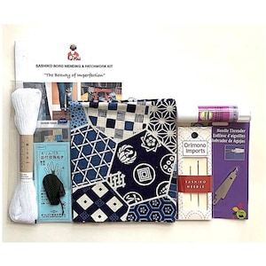 May include: A Sashiko Boro mending and patchwork kit with the text "The Beauty of Imperfection". The kit includes white thread, needles, a needle threader, and a patchwork fabric with blue and white geometric patterns.