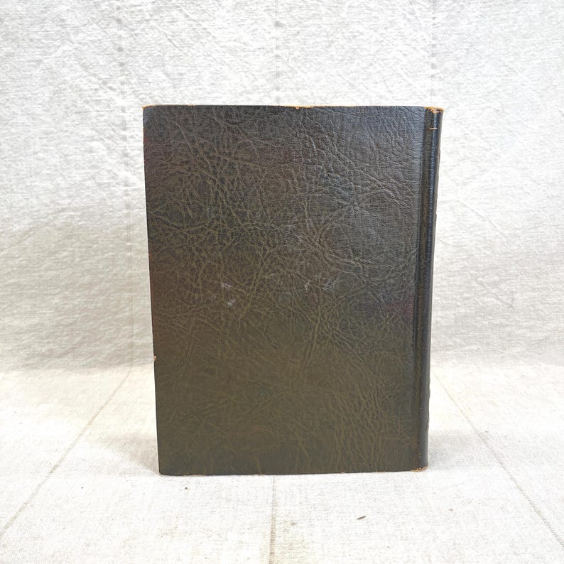 May include: A vintage book with a dark green, textured cover. The spine is visible, showing the aged edges of the pages. The book is standing upright, showcasing its worn, classic appearance.