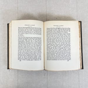 May include: Open book with text about Franz Liszt, a famous composer. The pages are aged, with black text on a cream background. The book is open on a light-colored surface.