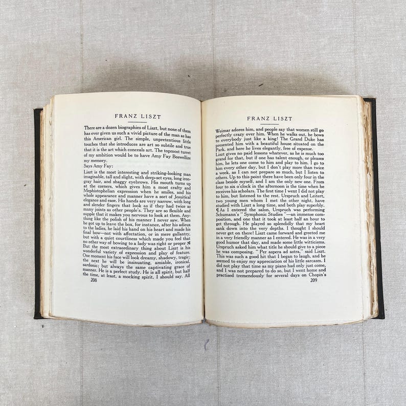 May include: Open book with text about Franz Liszt, a famous composer. The pages are aged, with black text on a cream background. The book is open on a light-colored surface.