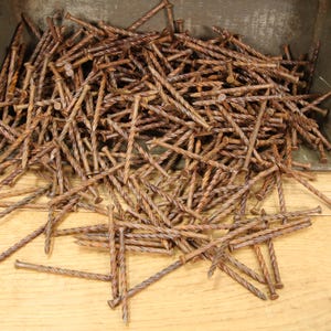 May include: A large pile of rusty, twisted nails in a metal container. The nails are scattered on a wooden surface.