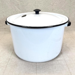 May include: A white enamel pot with a black rim and handles, and a matching lid with a black knob. The pot has a classic, vintage design, suitable for cooking and serving.