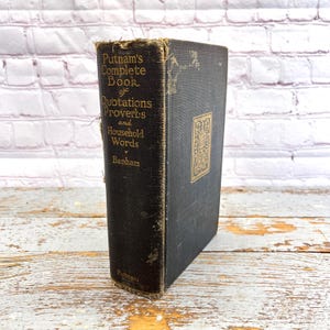 May include: A vintage hardcover book titled "Putnam's Complete Book of Quotations, Proverbs and Household Words" by Benham. The book has a dark cover with gold lettering and a decorative emblem. The edges show signs of wear.