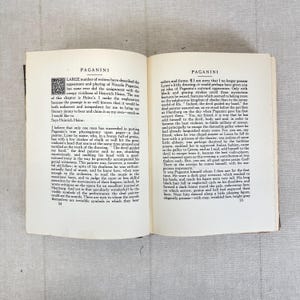 May include: Open book pages with text about Paganini, featuring a decorative initial. The text is in English, with a focus on the appearance and playing of Niccolo Paganini. The pages are aged, with a light beige tone.