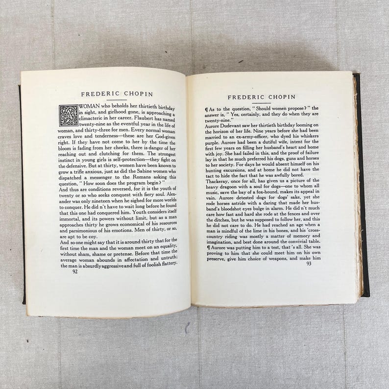May include: Open book with text titled "FREDERIC CHOPIN" on both pages. The left page has text about a woman's thirtieth birthday. The right page discusses women proposing. The pages are aged with a dark binding.