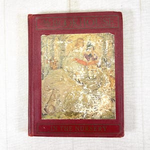May include: A vintage hardcover book titled The Bookhouse In The Nursery with a deep red cloth cover. The front features an inset illustration of two children in a forest setting surrounded by woodland animals, including a rabbit and a squirrel.