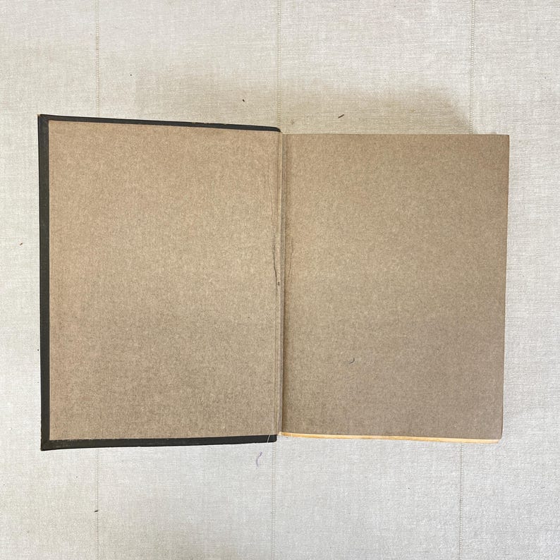 May include: An open book with a dark brown cover and light brown pages. The pages are blank and ready for writing or drawing. The book is lying on a light-colored surface.