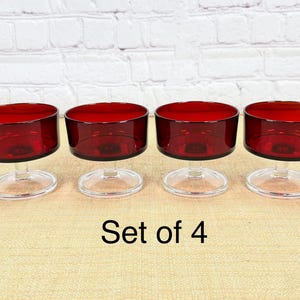May include: Set of four vintage red glass dessert dishes. Each dish features a cylindrical red bowl atop a clear, stemmed base. The text "Set of 4" is visible in the image.