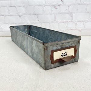 May include: A long, rectangular metal storage bin with a rusty brown handle and a white label with the number "42" on it.
