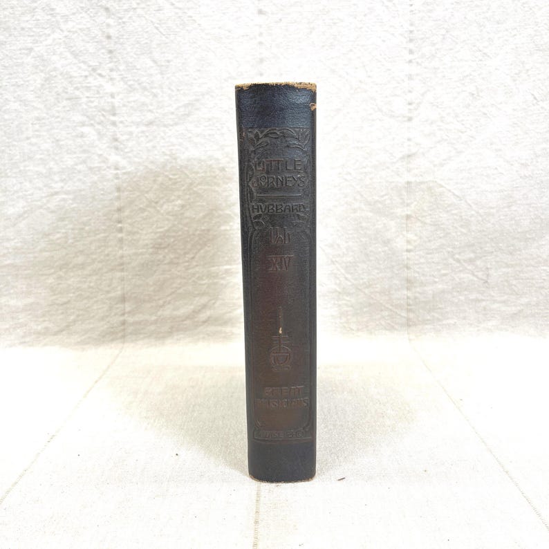 May include: A vintage book spine with embossed text. The title "Little Journeys" is visible, along with the author's name, Hubbard, and the volume number, XII. The spine is dark brown with gold lettering.