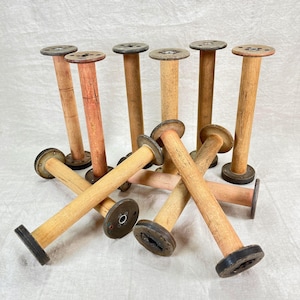 May include: A collection of vintage wooden spools. The spools have a cylindrical body with a circular top and bottom. The wood has a natural, aged appearance with variations in color, ranging from light tan to reddish-brown. The metal ends show signs of wear.