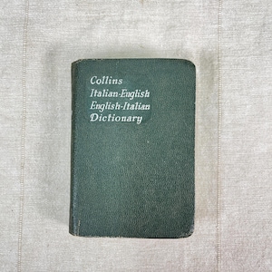 May include: A small, dark green Collins Italian-English, English-Italian Dictionary. The book has a textured cover and white text on the front that reads "Collins Italian-English English-Italian Dictionary."