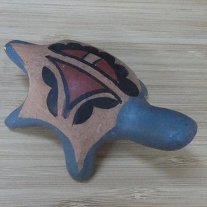 May include: A small, hand-painted ceramic turtle figurine with a blue underside and a brown, black, and red design on the top.