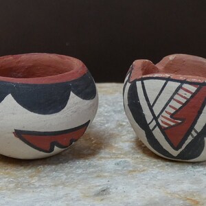 May include: Two small, hand-painted pottery bowls with geometric designs. One bowl is white with black and red accents, the other is white with black, red, and white accents.