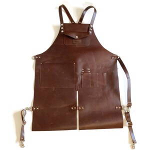 May include: A brown leather apron with multiple pockets and adjustable straps. The apron has a small pocket on the chest with the text "F&G" printed on it.