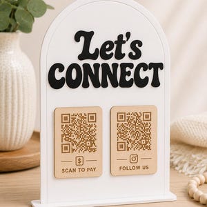 May include: A white arched sign with black raised lettering that reads Let's CONNECT. Two light wood rectangular plaques are attached, each featuring a QR code. The left plaque has a dollar sign icon and the text SCAN TO PAY, while the right plaque has an Instagram icon and the text FOLLOW US.