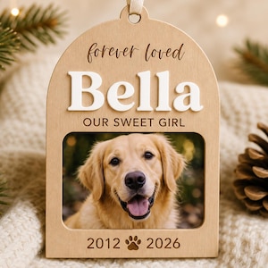 May include: An arched wooden ornament featuring the text "forever loved", the name "Bella" in raised white letters, and the phrase "OUR SWEET GIRL". Below is a photo of a golden retriever and the engraved dates "2012" and "2026" with a paw print.
