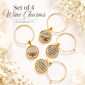 May include: A set of four gold-toned wine charms featuring circular pendants with printed text from 1 Corinthians 13. Each charm consists of a thin gold hoop attached to a round bezel containing paper inserts with black text and small floral accents.