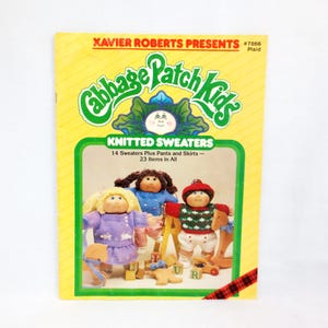 Könnte beinhalten: Ein Vintage-Buchcover von Cabbage Patch Kids, gelb mit grünem Rand, mit dem Text "KNITTED SWEATERS". Das Cover zeigt Illustrationen von drei Cabbage Patch Kids-Puppen in Strickpullovern. Das Buch trägt den Titel "Xavier Roberts Presents."