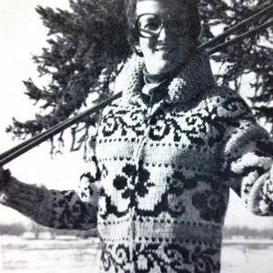 May include: A black and white photo of a person wearing a white and black patterned sweater. The person is holding a ski pole in their right hand and is standing in front of a tree.