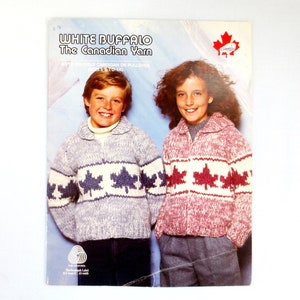 Puede incluir: Un folleto de patrones de tejido de punto con un niño y una niña que llevan suéteres con un diseño de hoja de arce. El folleto se titula "White Buffalo The Canadian Yarn" e incluye instrucciones para un cárdigan o un jersey para las tallas 2 a 14.