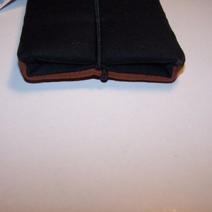 May include: A black zippered pouch with a brown trim. The pouch is closed and lying flat on a white surface.