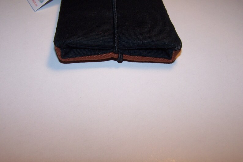May include: A black zippered pouch with a brown trim. The pouch is closed and lying flat on a white surface.